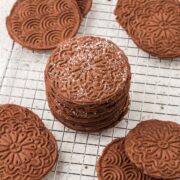 Chocolate pizzelles stacked on a cooling rack.