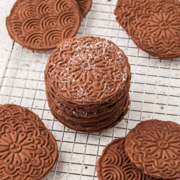 Chocolate pizzelles stacked on a cooling rack.