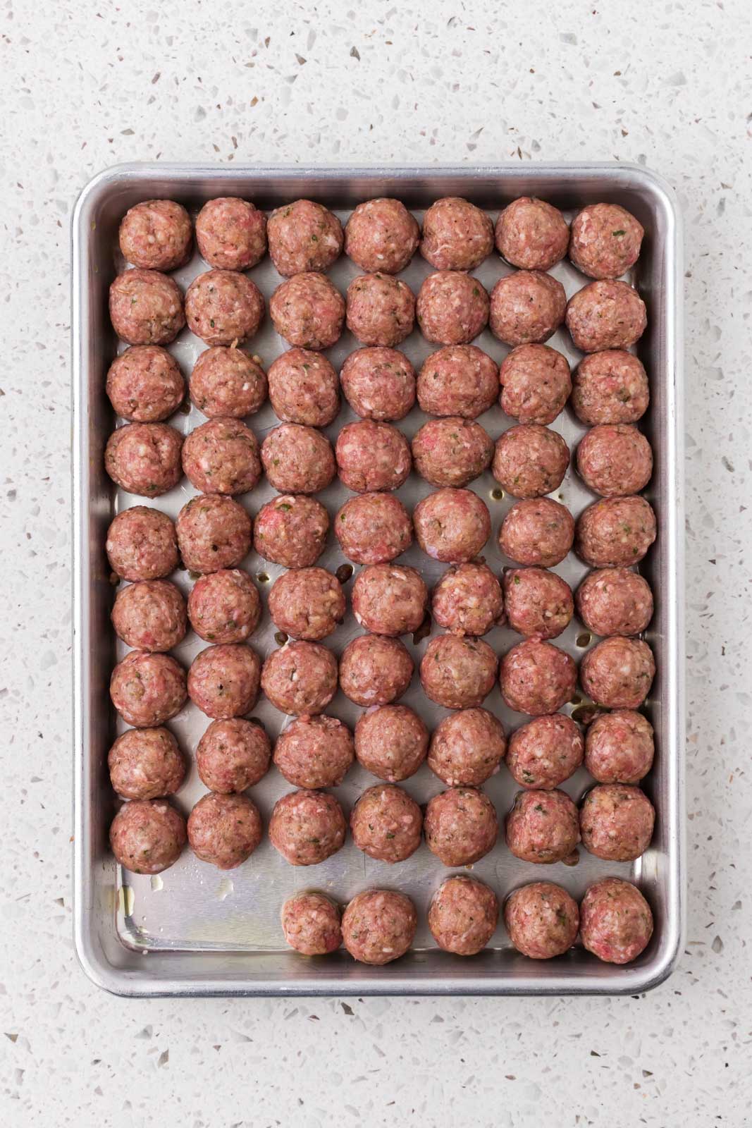 Rolled meatballs on a baking sheet with olive oil.
