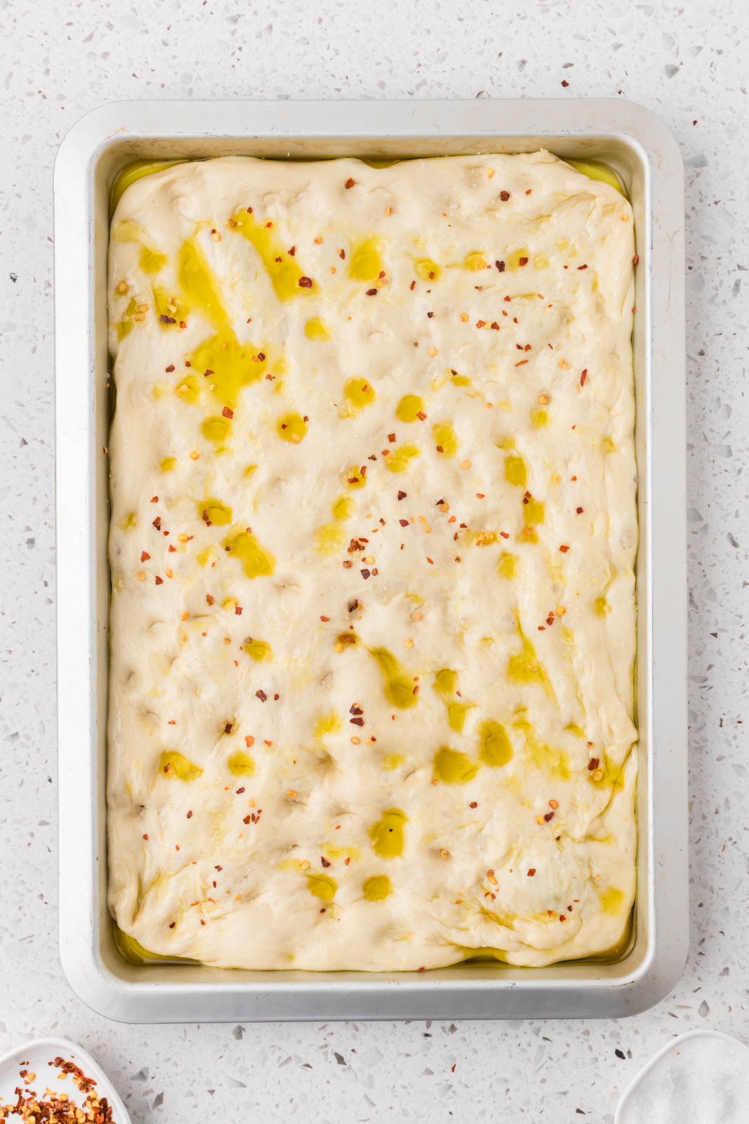 Focaccia dough with salt and crushed red peppers sprinkled on top.