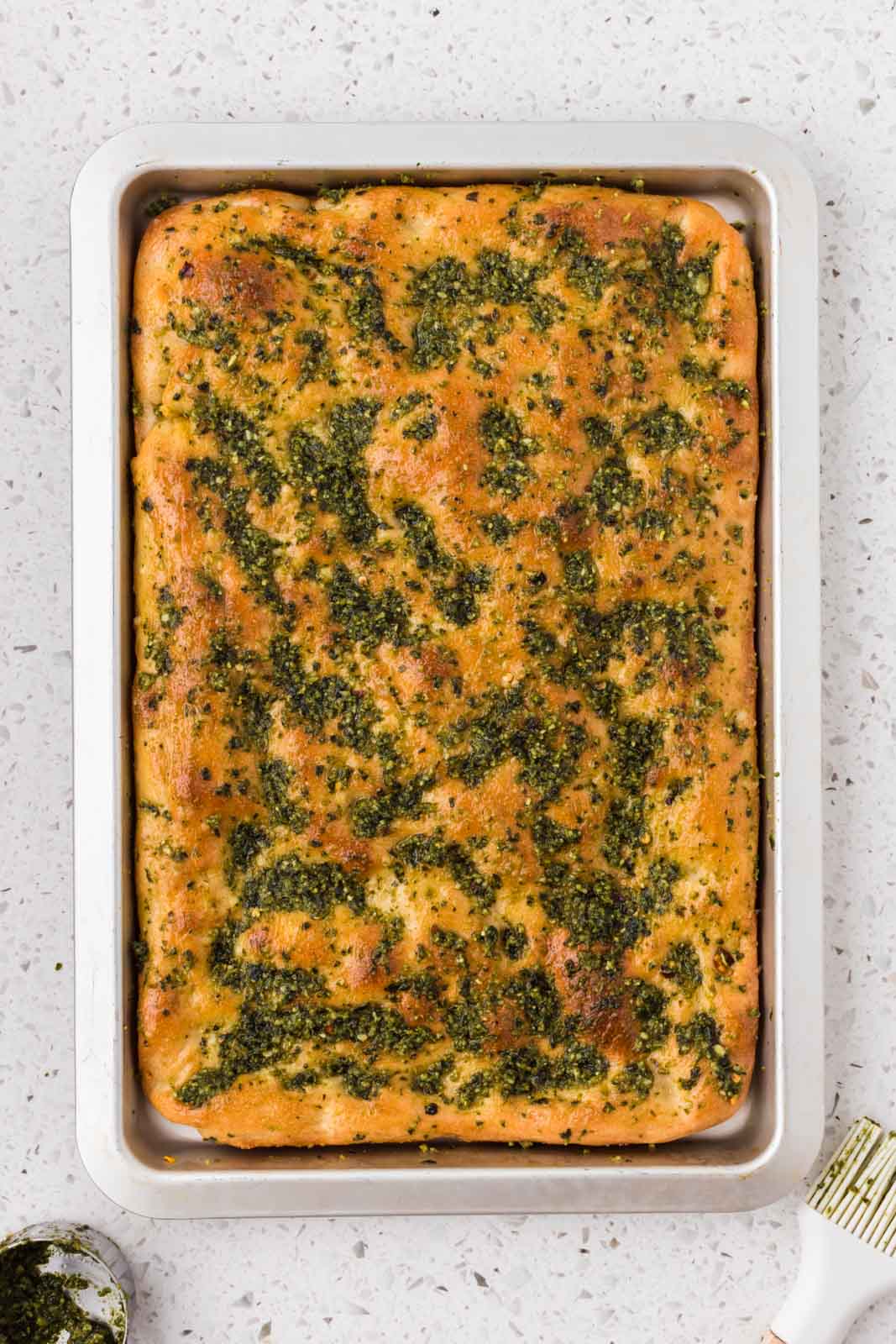 Baked focaccia with pesto sauce brushed on top.