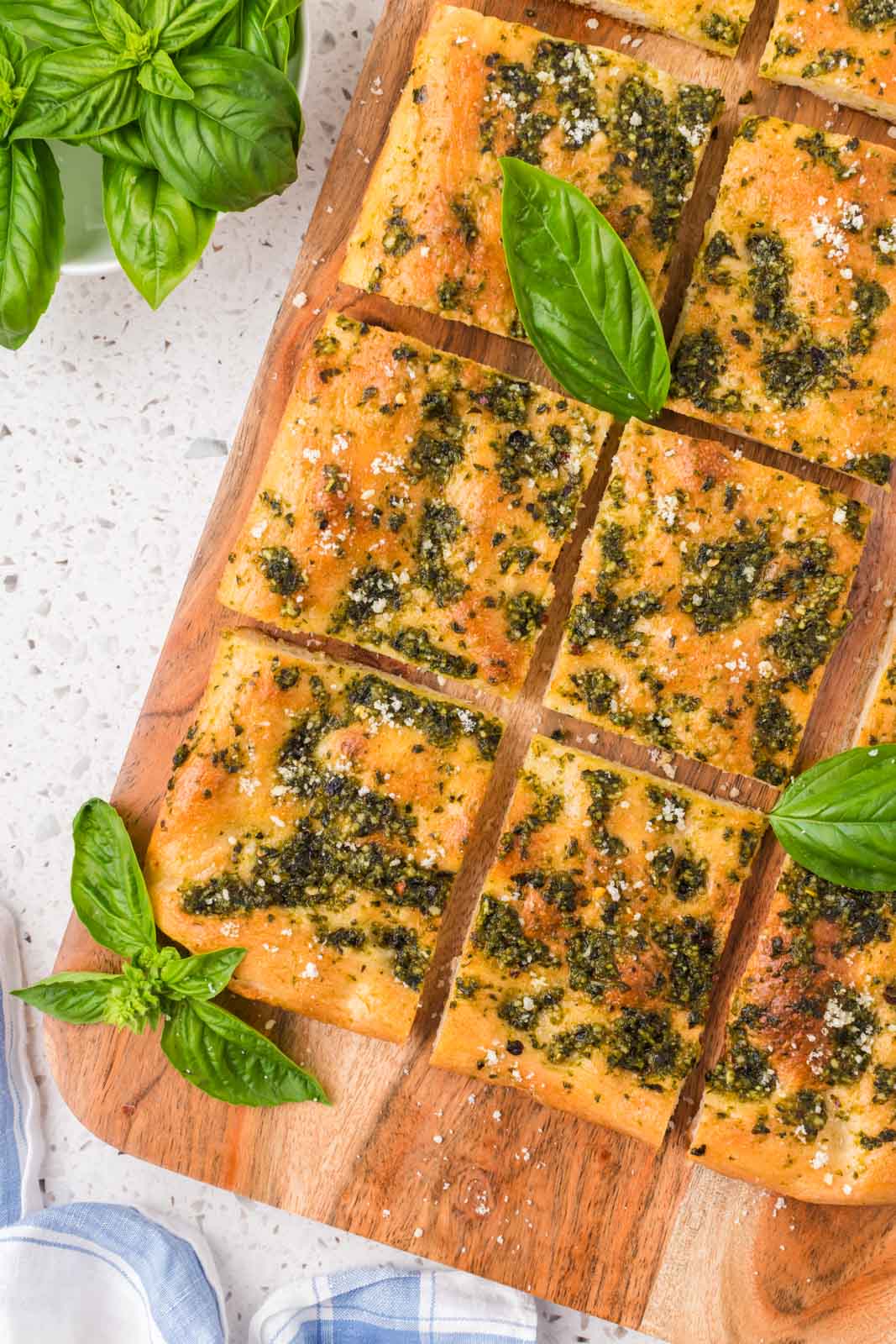 Pesto focaccia on a serving board garnished with grated parmesan and fresh basil leaves.