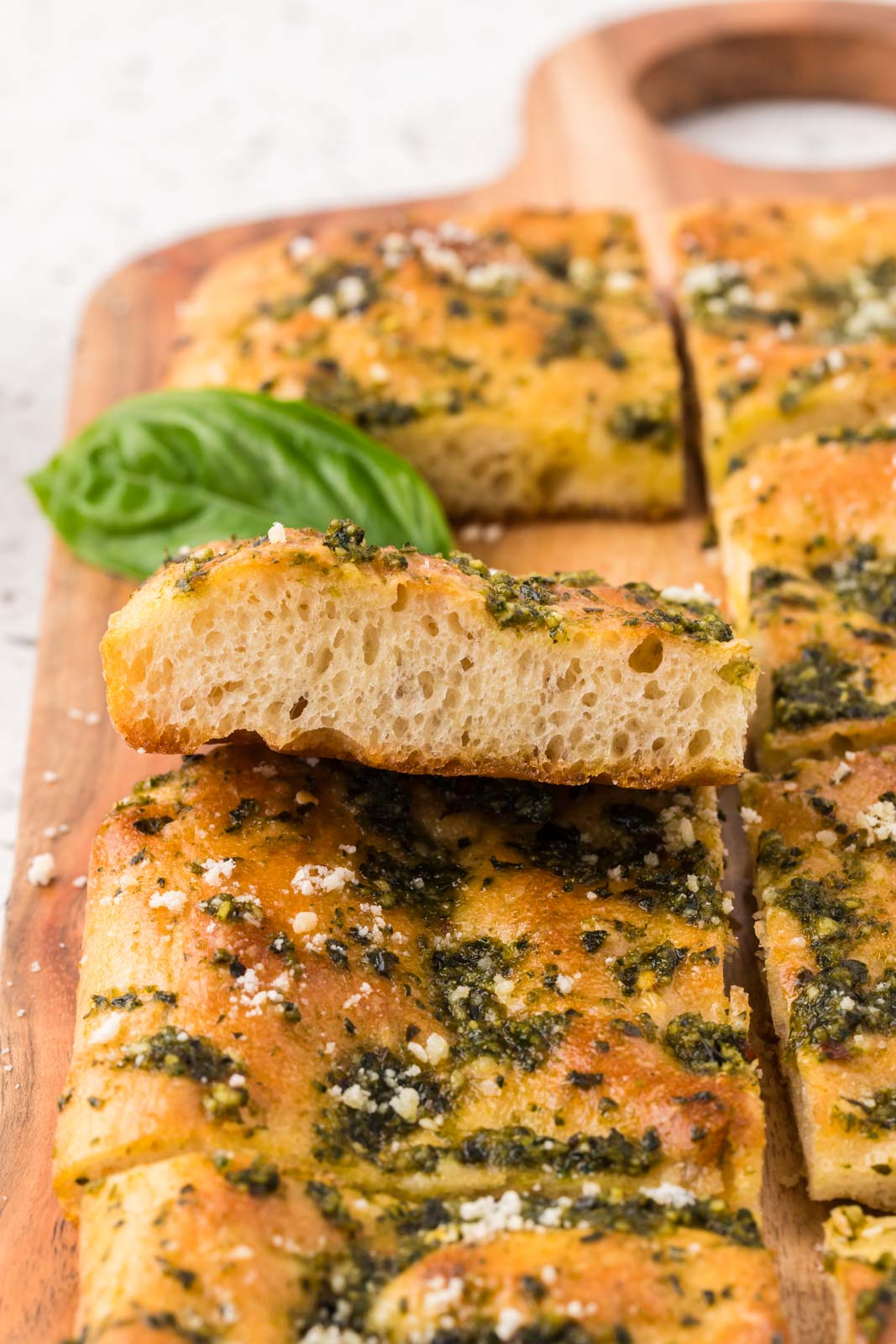 Pesto focaccia on a wooden board garnished with parmesan cheese.