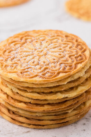 Pizzelle stacked on the counter, sprinkled with powdered sugar.