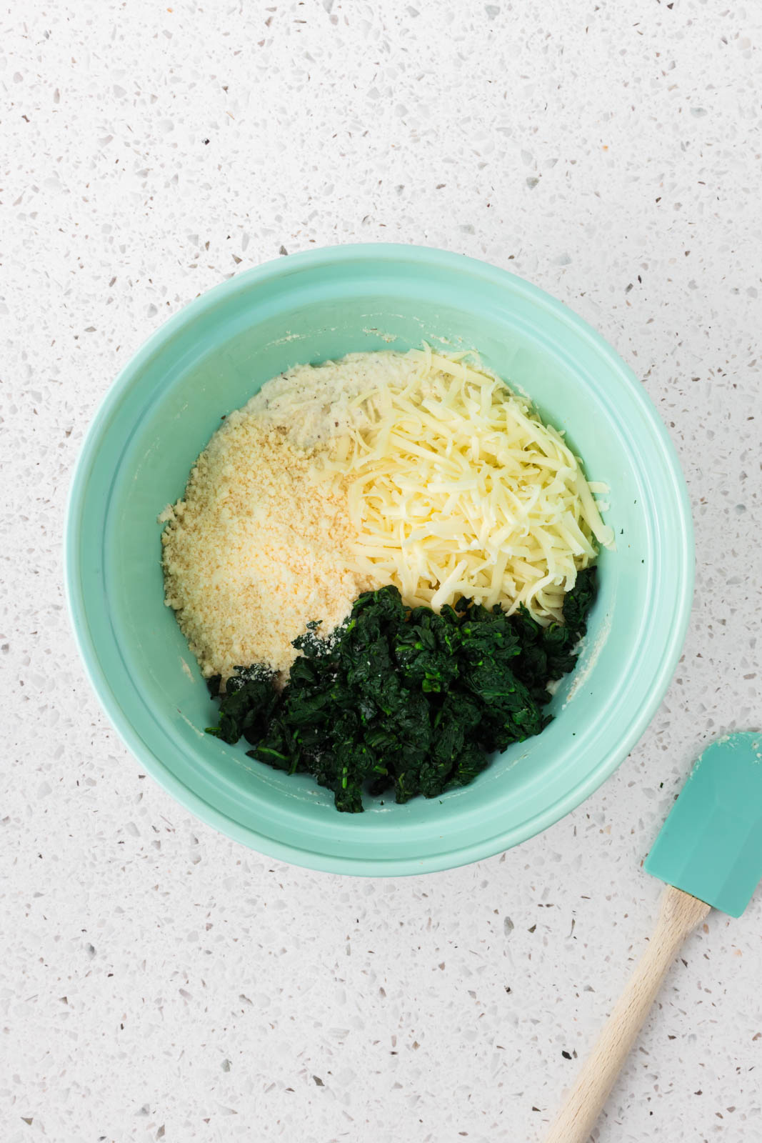 Spinach, parmesan, ricotta, and mozzarella in a mixing bowl.