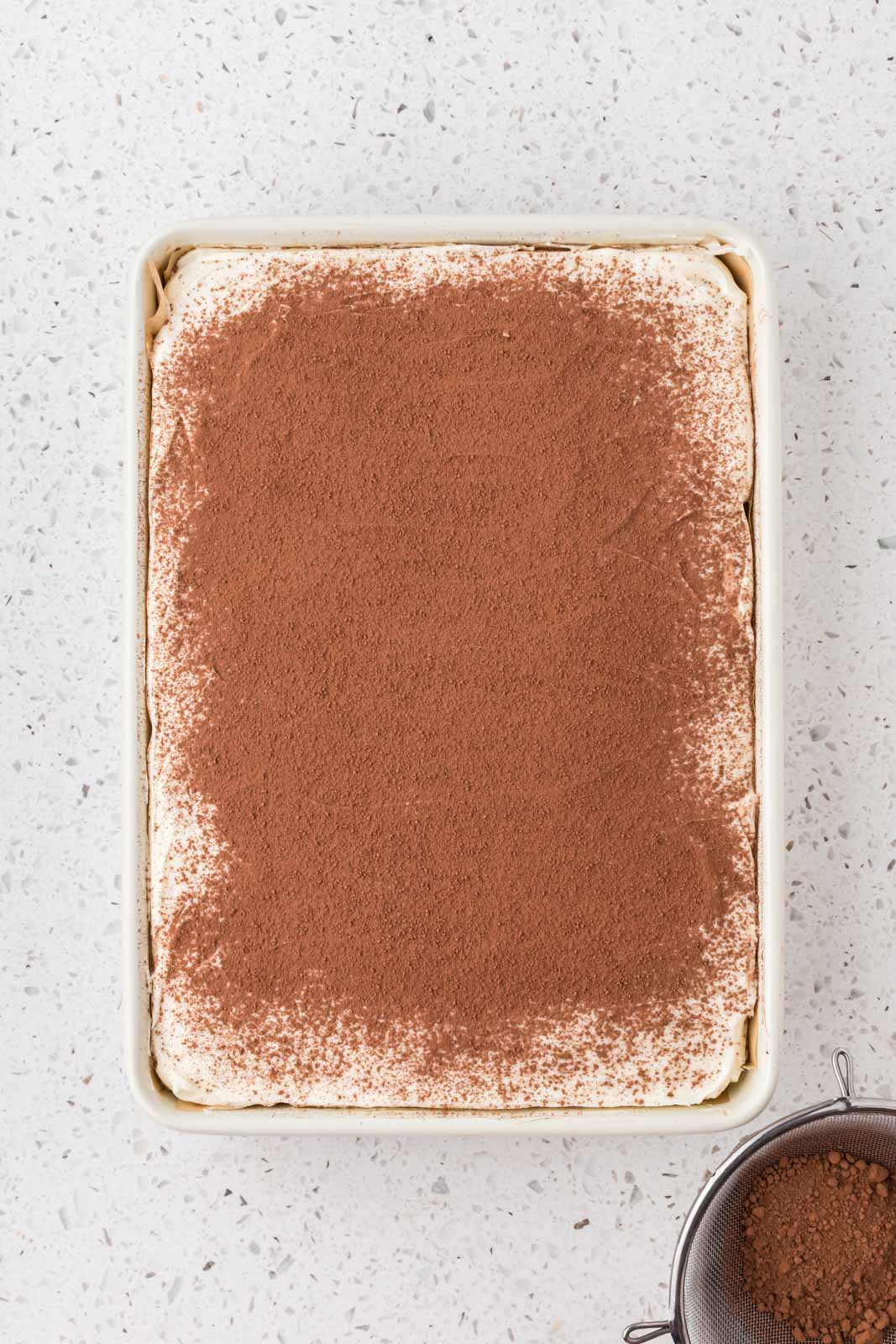 Tiramisu poke cake with cocoa powder sprinkled over the top evenly.