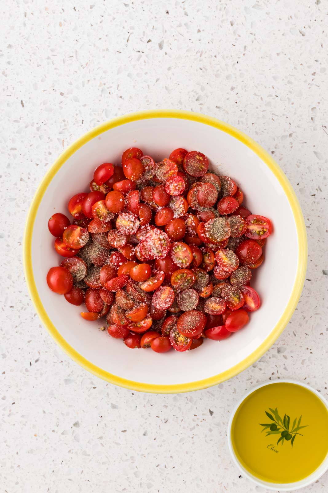 Halved cherry tomatoes in a bowl with seasonings.