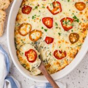 Baked spicy spinach artichoke dip in a casserole dish with a spoon.