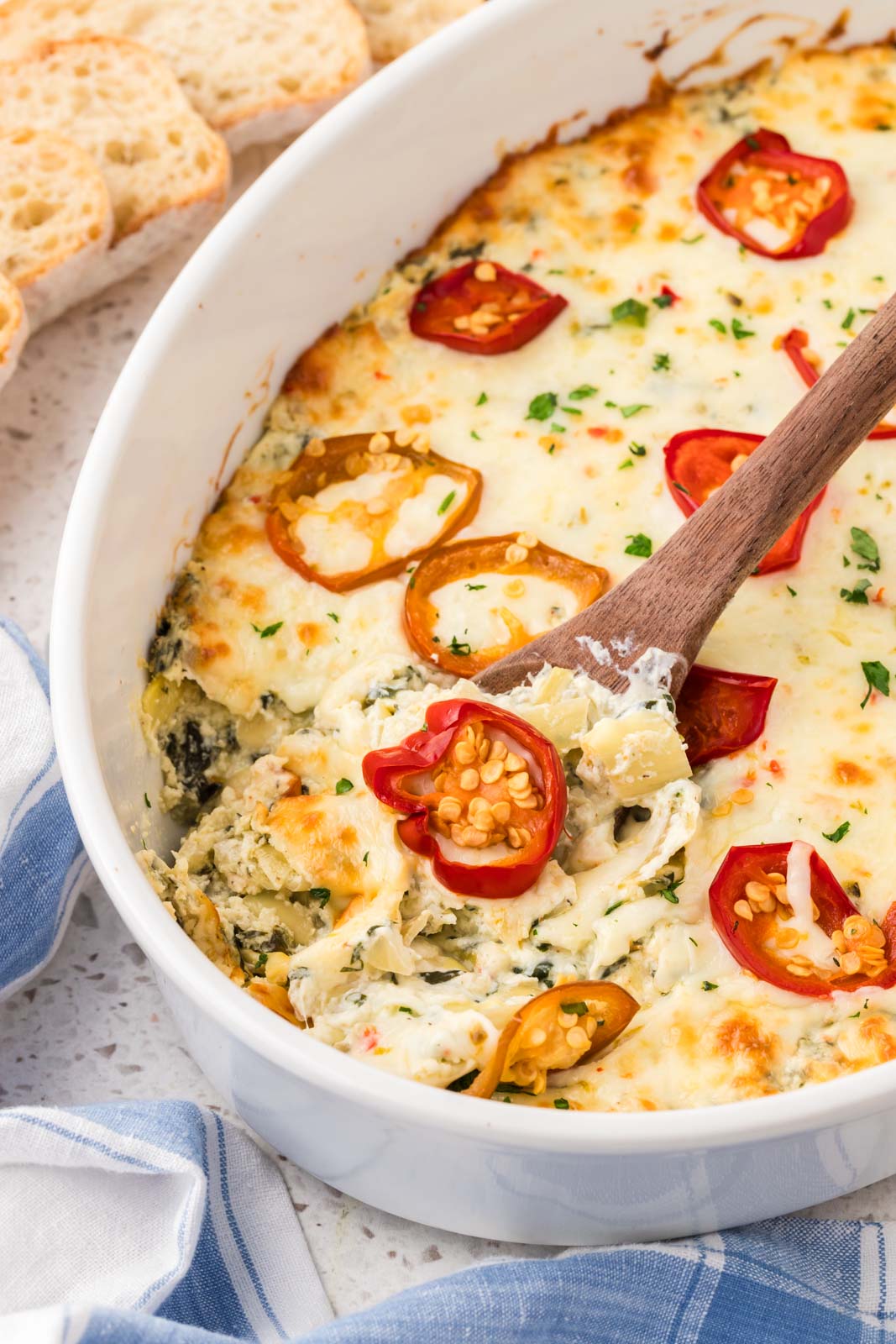 Spicy spinach artichoke dip in a casserole dish with a wooden spoon. 