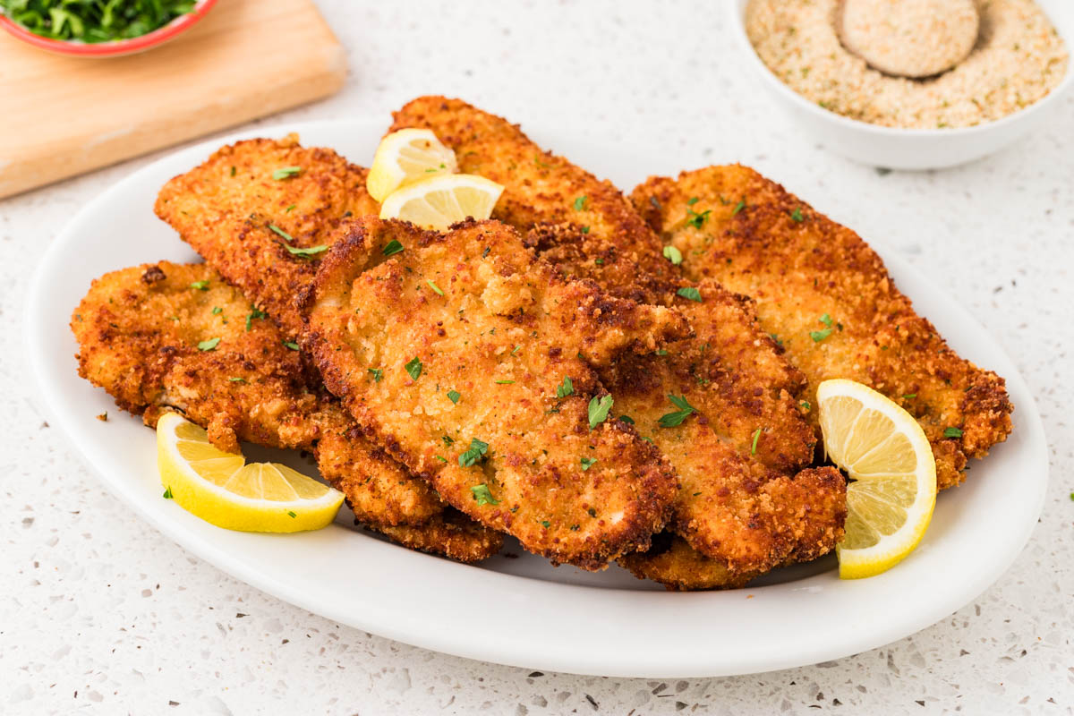 Italian chicken cutlets on a platter with lemons.