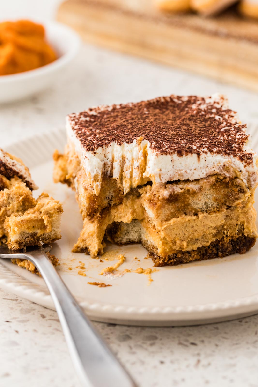 Pumpkin tiramisu on a plate with a bite taken out. 